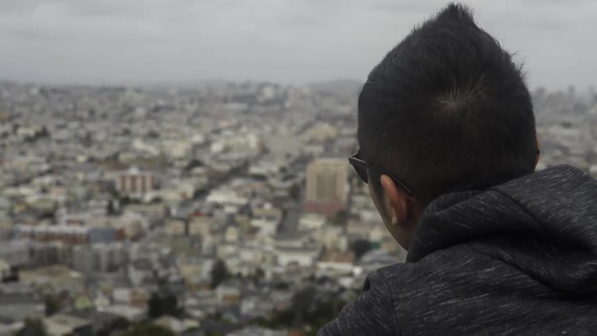 Person in sunglasses looking out over city skyline with thoughtful reflective vibe.
