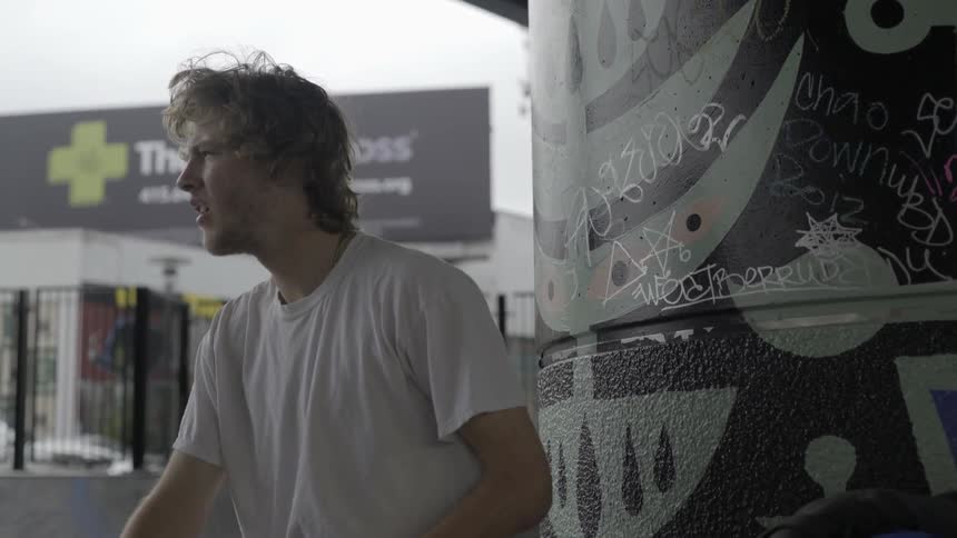 A man stands against a column at an urban skate park