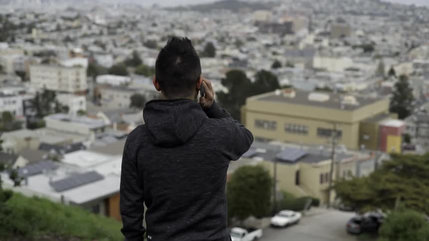 A man is talking on a phone while standing on a hill over a town
