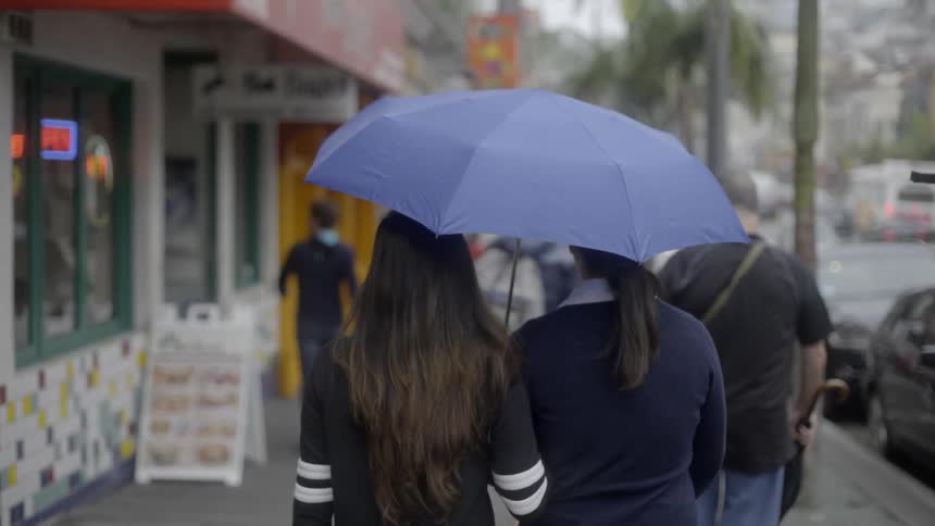 People walking down wet sidewalk on rainy day with calm everyday rhythm.