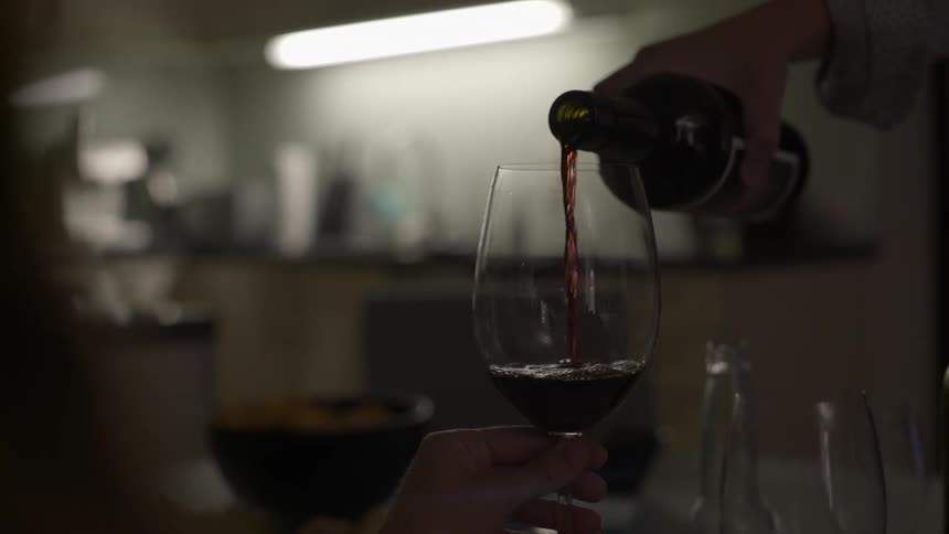 Woman elegantly pouring wine into glass with warm refined lifestyle feel.