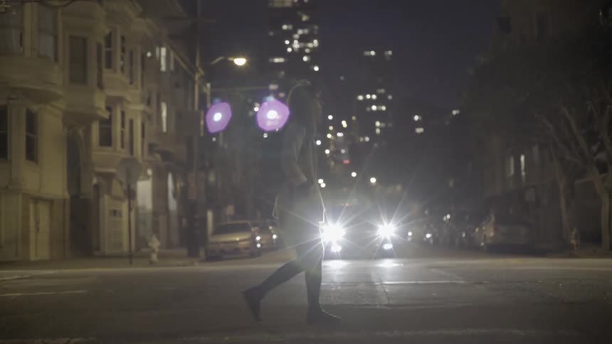 Woman crossing urban street at night with reflective cinematic city mood.