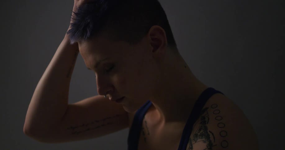 A tattooed woman in a tank top sits looking down