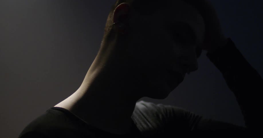A dancer lowers his head in light and shadow