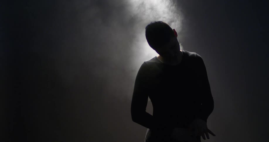 A person stands in the shadows as smoke floats by