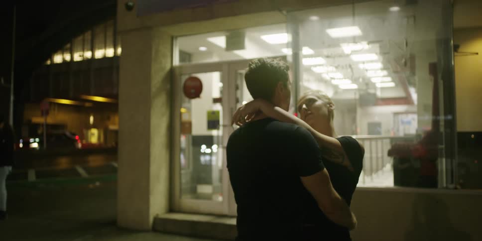 A man and a woman embrace outside a store at night