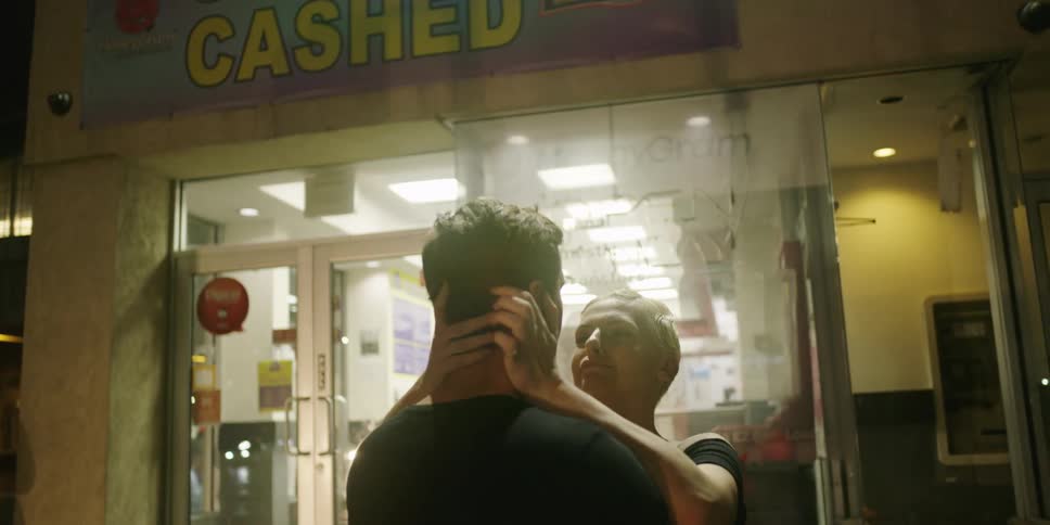 A man and woman stand outside and hug and laugh
