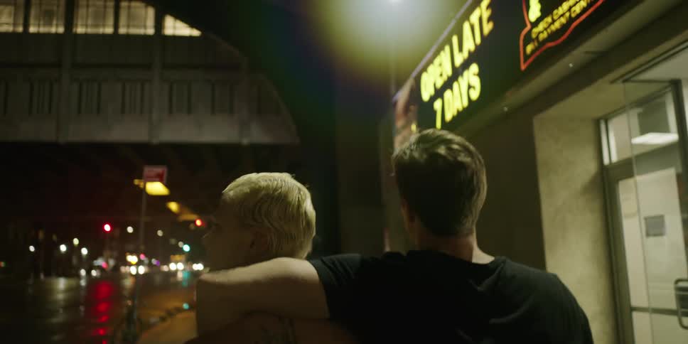 A couple walk down the sidewalk past city storefronts at night