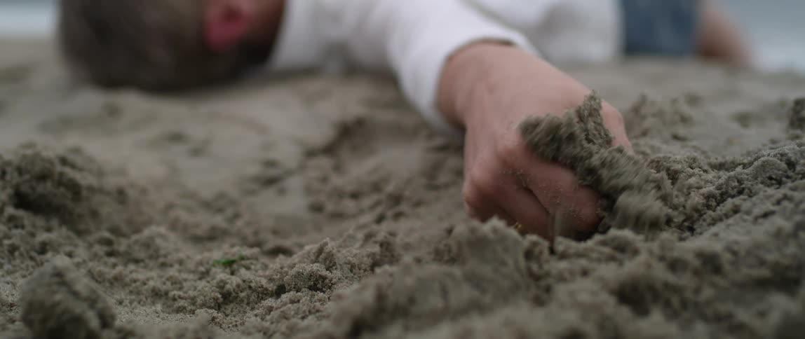 A person lays in the sandy beach and plays with the sand in between their fingers