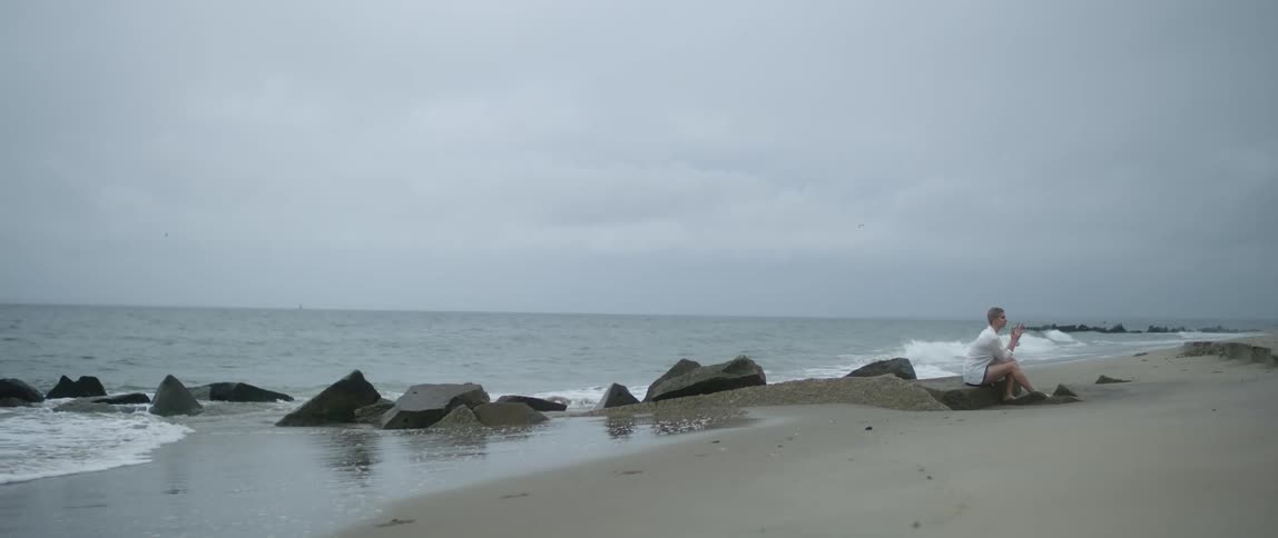 Barefoot woman sitting on the rocks of a beach next to the ocean
