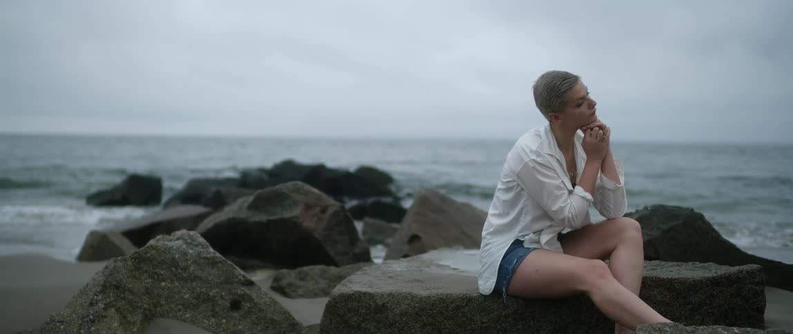 A woman is sitting on a rock by the coast of an ocean