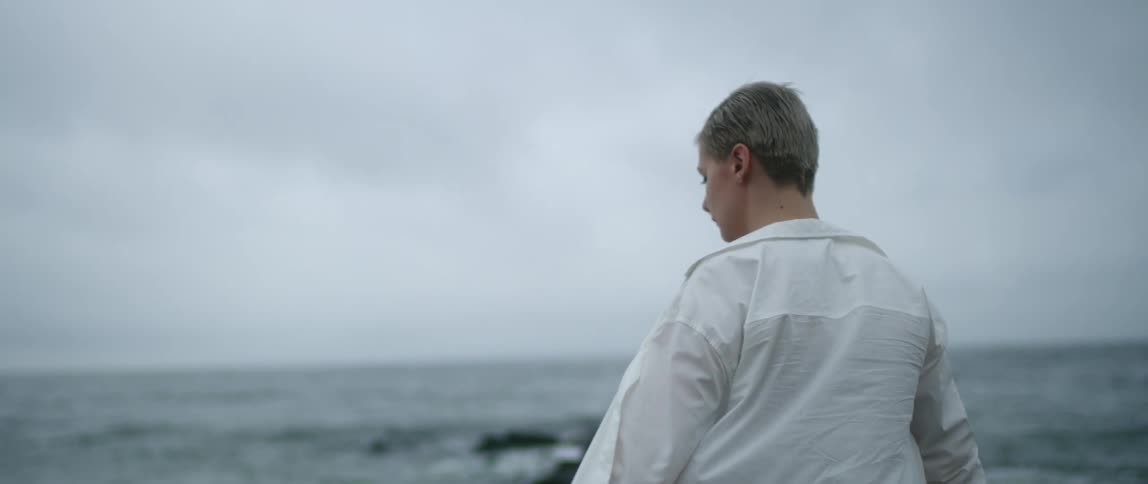 A woman stands on the shore and looks out at the water