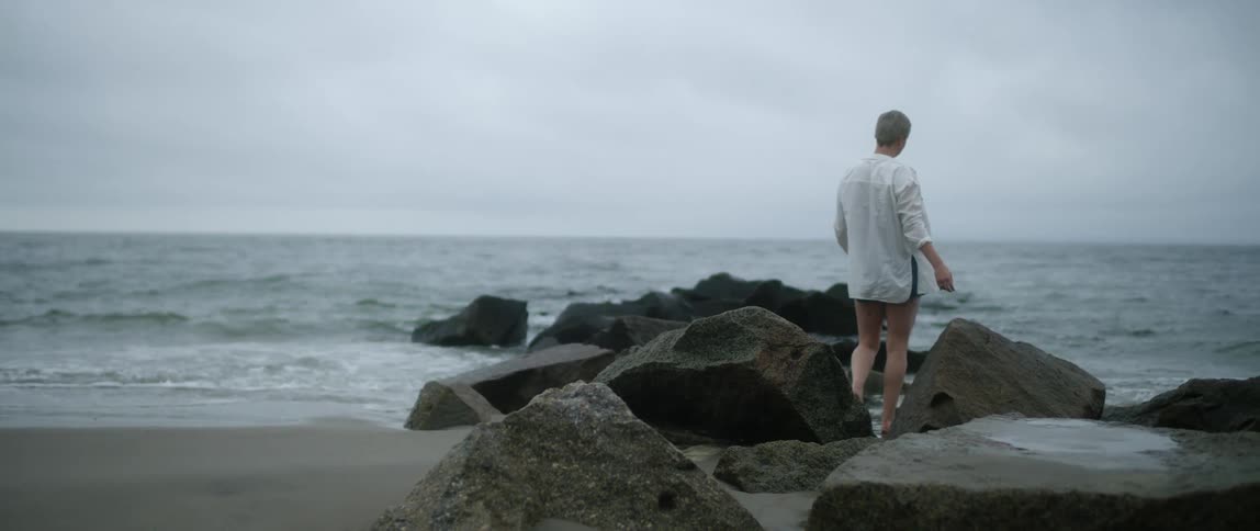 A white woman walks on the beach among rocks