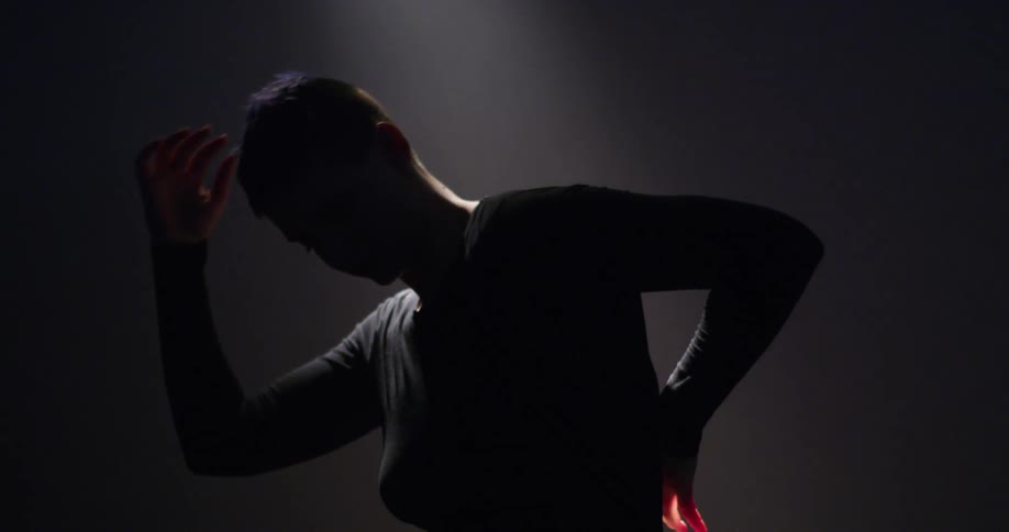 Dancer bends and stretches dimly lit by light