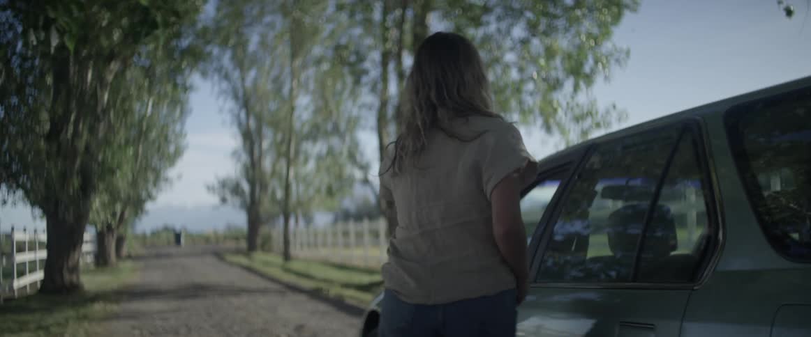 Two woman hug each other standing in a rural home driveway and then one gets into their vehicle
