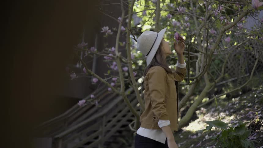Woman reaching to smell flower on tree with gentle peaceful nature moment.