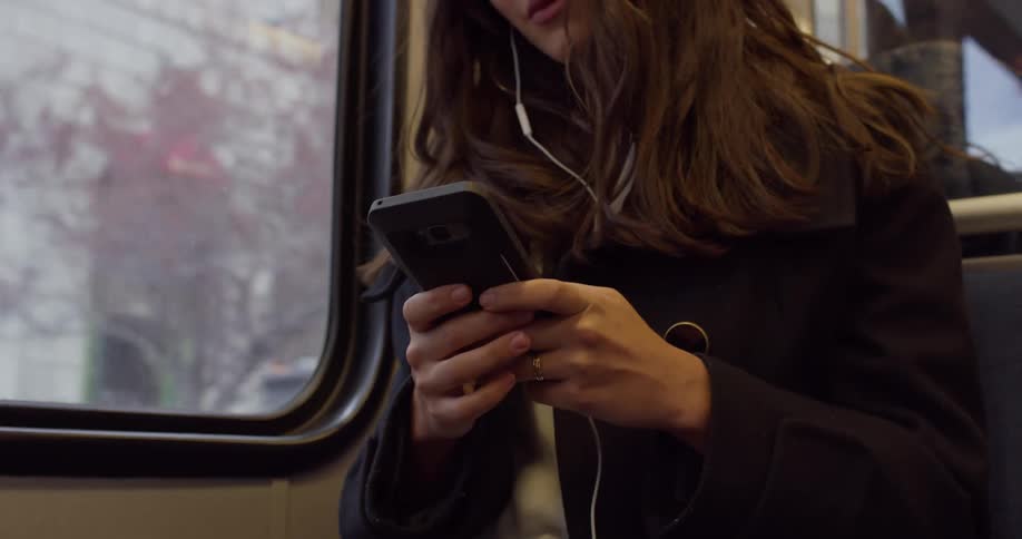 A woman sits on a subway and uses her cell phone