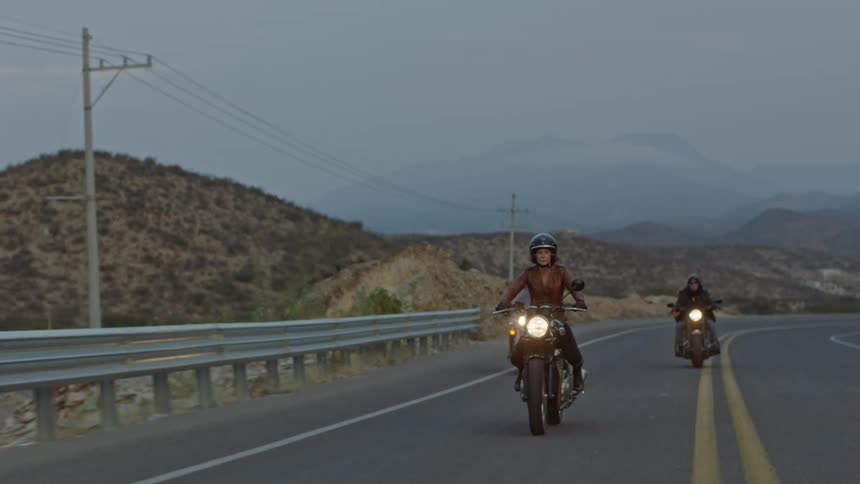 Three people drive motorcycles down a street