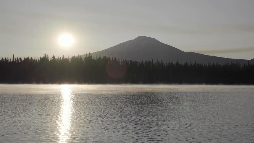 Lake surrounded by pine forest near mountain at sunset