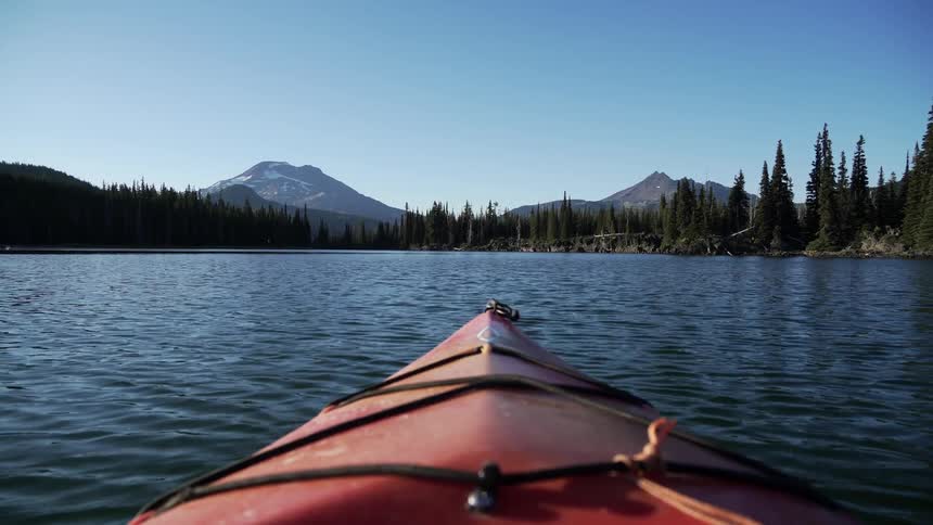 Point of view front of kayak while kayaking in a lake surrounded by pine trees