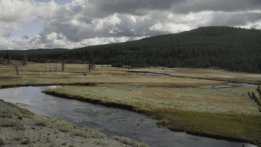 A narrow creek runs through a field near hills