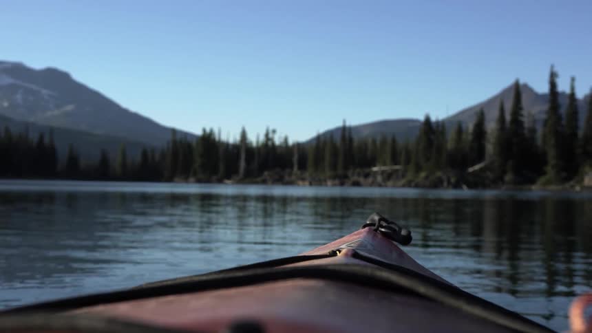 Point of view from kayak in a lake facing pine trees and mountains