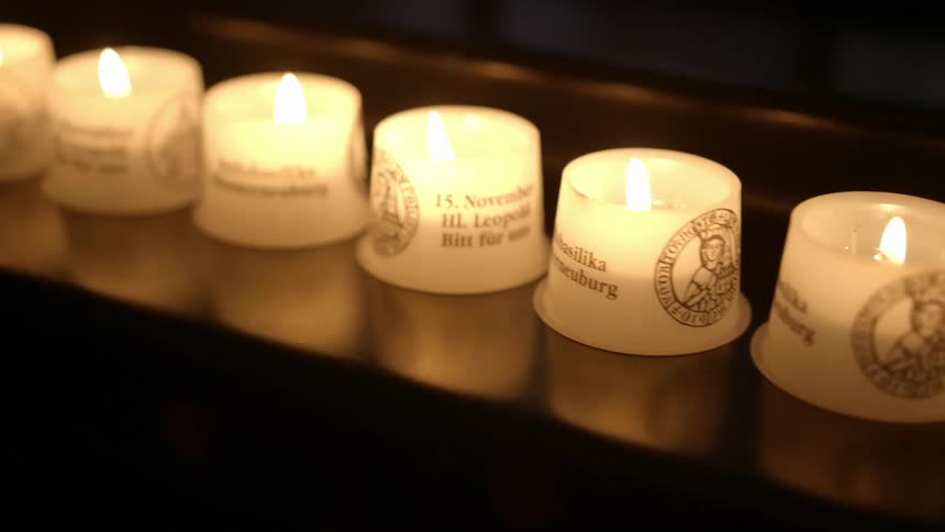 Row of small lit white candles reflect off glossy surface