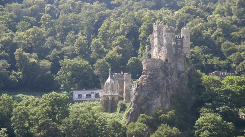 Two people walk toward a castle surrounded by a forest