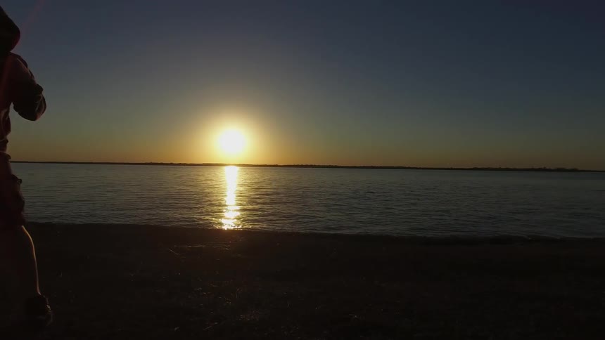 A man practicing boxing moves as the sun sets over the ocean