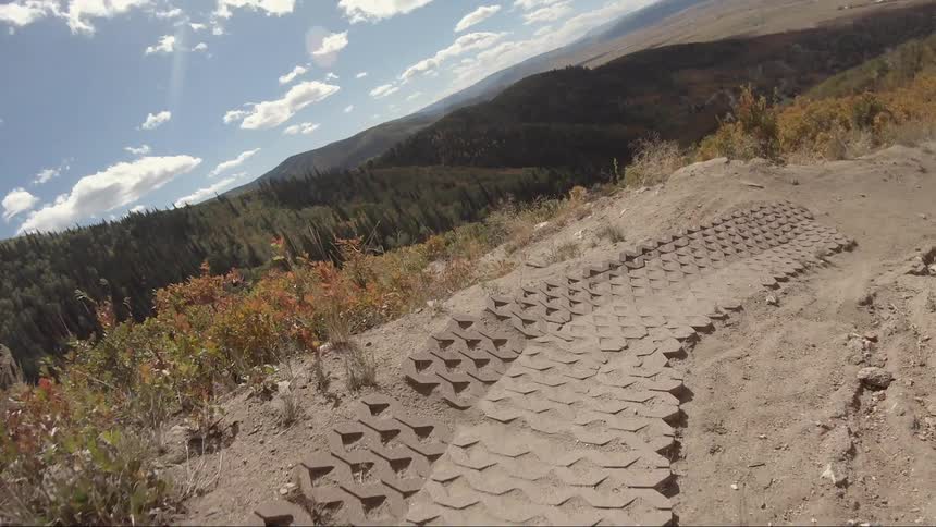 The shadow of a rider on a dirt bike is visible as the dirt track winds down a hill