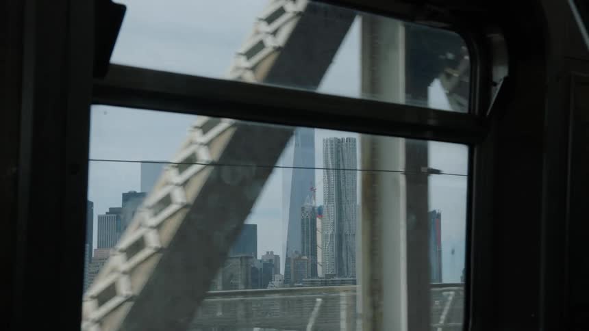 A commuter train travels over a bridge with a city skyline in the distance