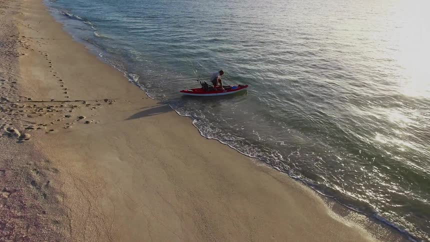 A person pulling a kayak across a beach and into the ocean