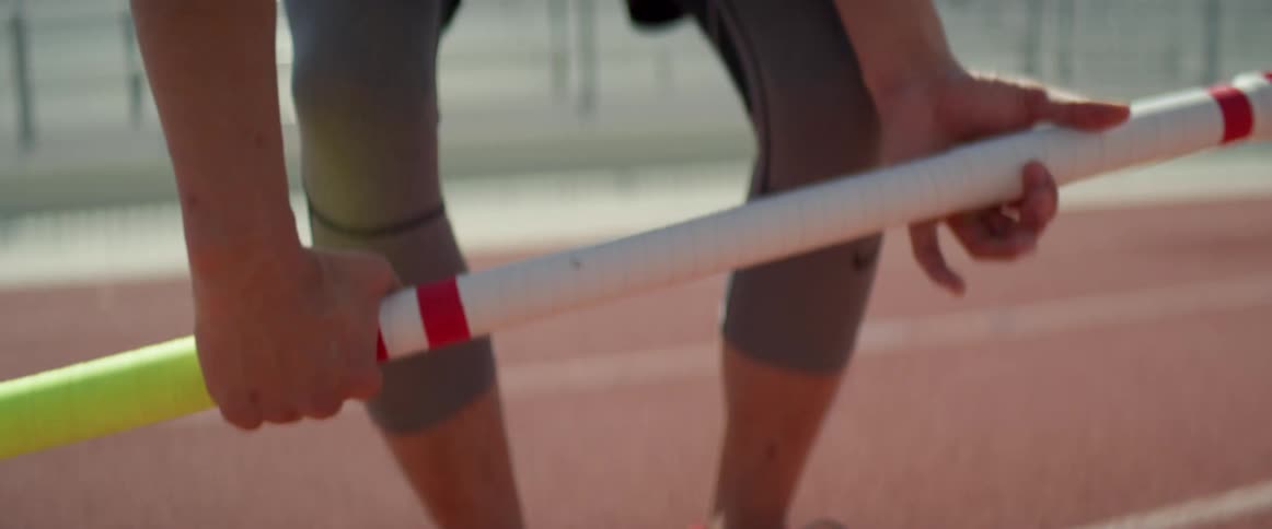 Man standing on the track of a stadium picks up vaulting pole from the ground