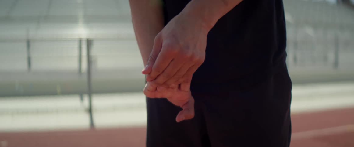 A person standing on a running track stretching their fingers