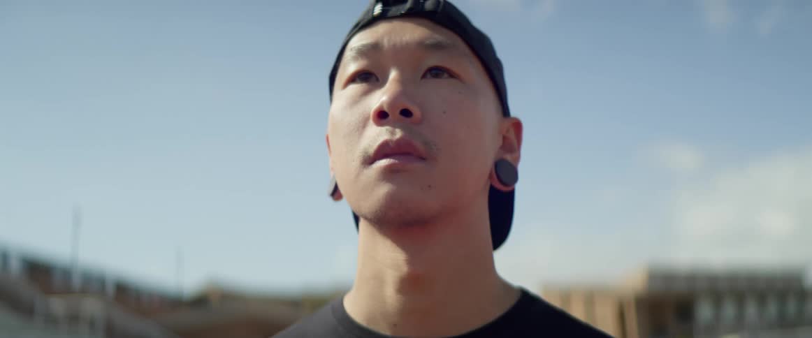 An asian man stands outside in a stadium and looks into the distance