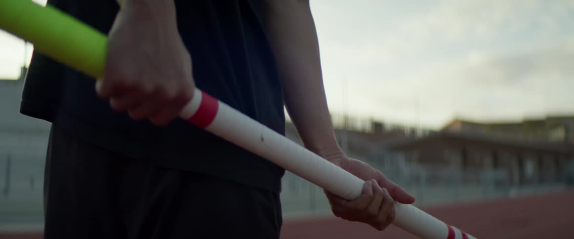 A person standing on a running track holding a pole