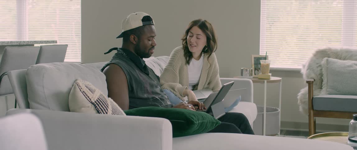 A man and woman sit on the couch together with their laptops