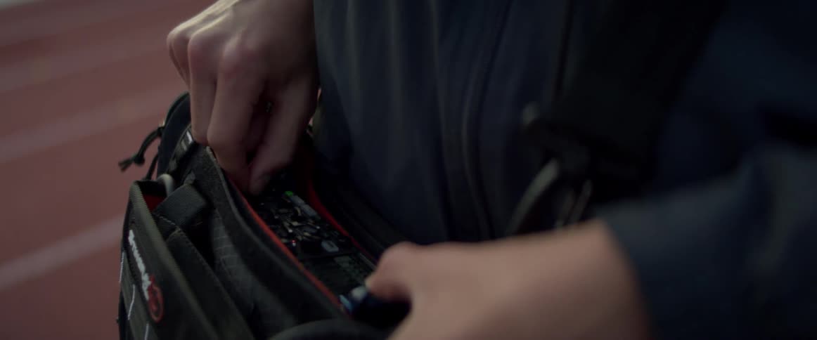 A worker carrying electronic filming and recording equipment in a bag adjusts the dials
