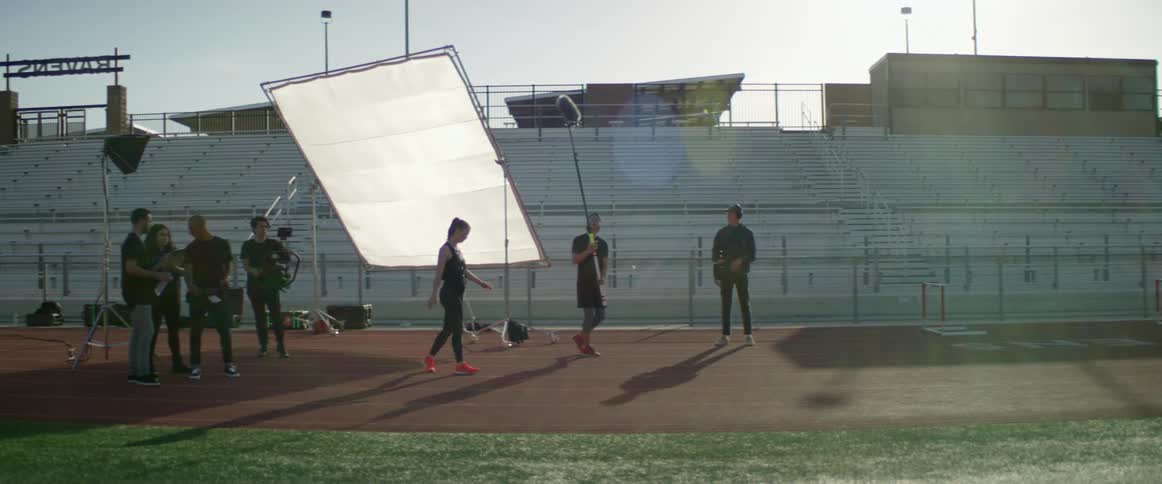 A film crew photographs and records a white female athlete walking in a stadium