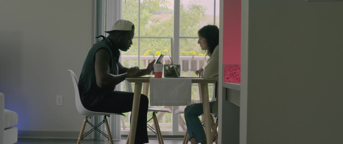 A man and woman sit at a table with their laptops and talk