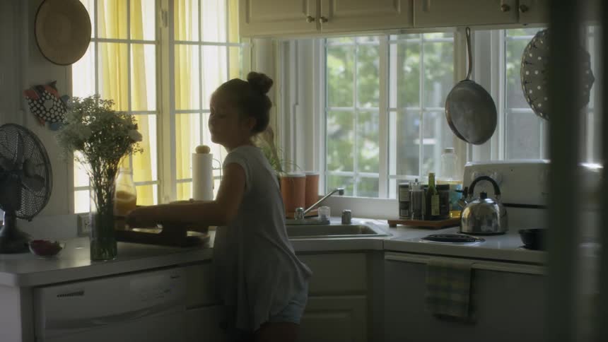 A girl picks up a tray and knocks a vase off the counter