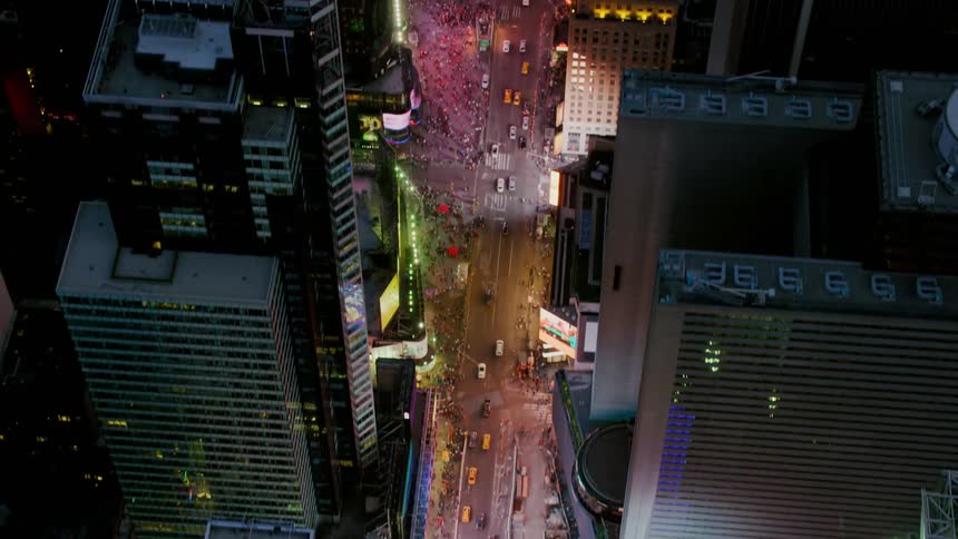 Cars and people fill a brightly lit area in a city downtown area