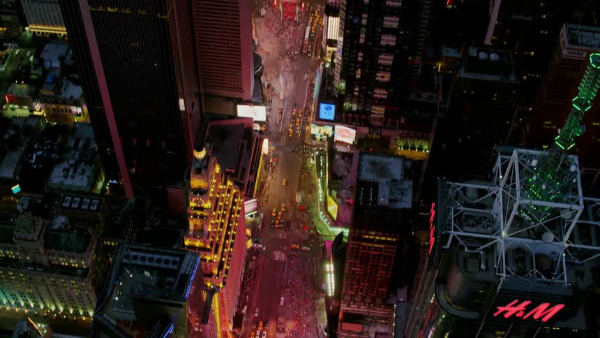 A city square is lit up with lights and screens in a downtown urban area