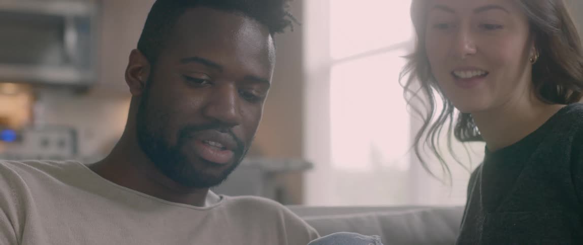 A black man sits on a couch and shows an asian woman a magazine