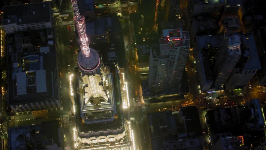 A tall skyscraper is lit up brighter than other buildings in a city at night