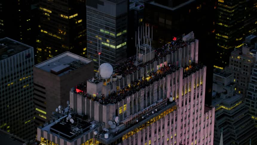 A large party is happening on the roof top of the tall building at night