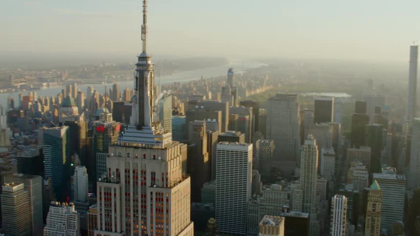 Empire state building towers over surrounding skyscrapers with river in the background