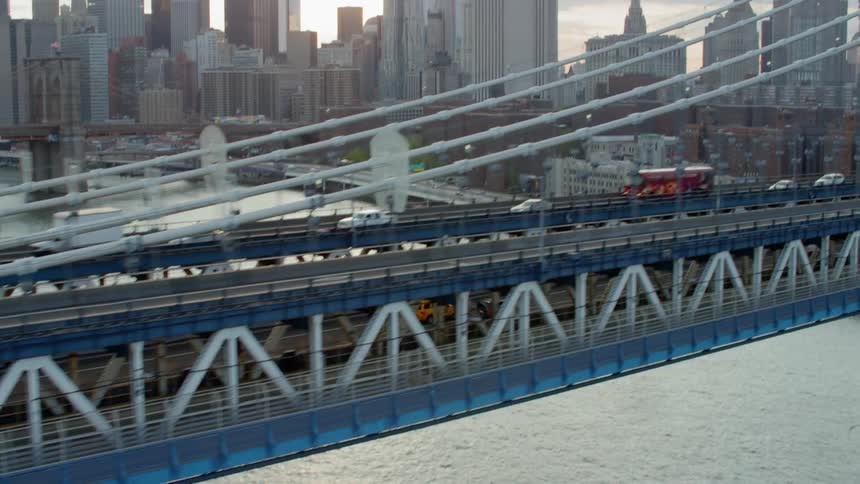 Cars and a bus drive across a suspension bridge in a city