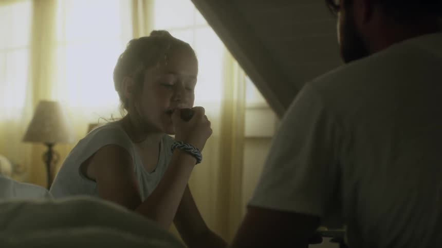A young girl eats a strawberry while a man talks
