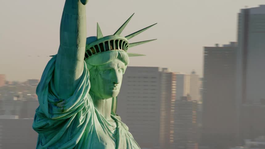 Downtown new york city is visible behind the statue of liberty